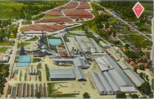 Aerial illustration of a large industrial lumber mill complex with rows of storage sheds, pools of water, and surrounding residential neighborhoods