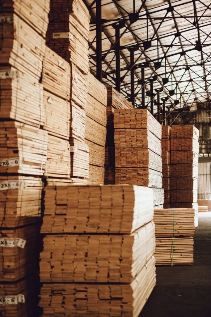 Large stacks of bundled lumber stored inside a warehouse, arranged in tall piles reaching near the ceiling